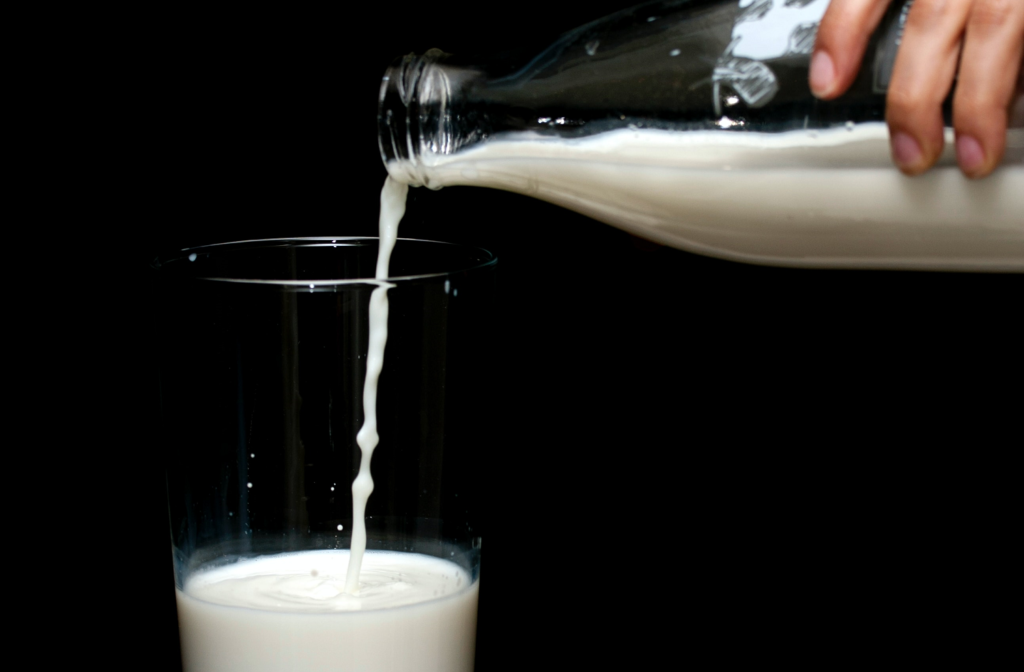 A hand pouring milk into a glass from an old-fashioned milk bottle.