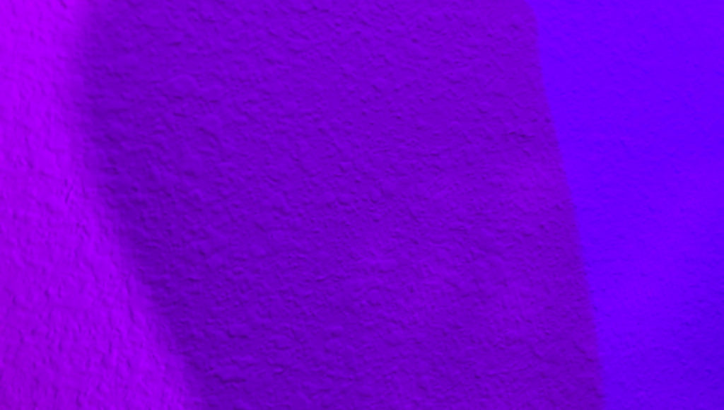 Converging colored lights (purple and blue) create a dark purple shade where they overlap on a wall.